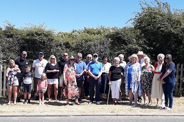 Some twenty local residents of Seaford, of all ages, standing at a roadside, in front of a tall hedge.