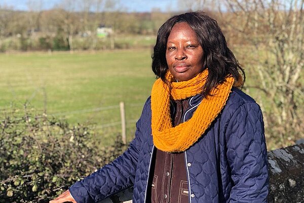 Councillor Janet Baah, with a prominent orange scarf, against a background of fileds, trees and sky.