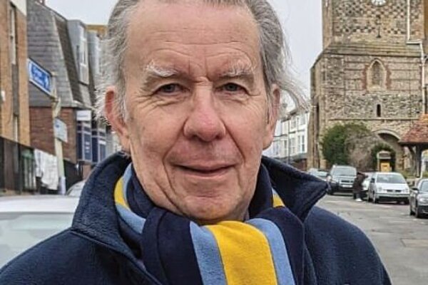 Head and shoulders shot of Stephen Gauntlett, with grey swept back hair. He is wearing a scarf with Ukrainian colours.