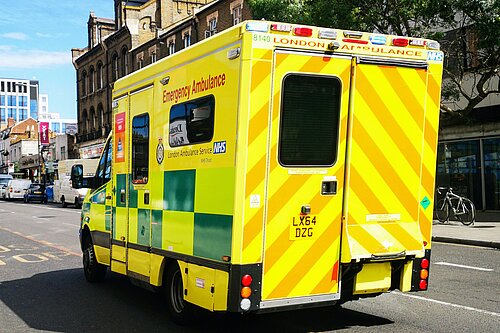 A street scene with a London ambulance in the foreground, taken from the rear.