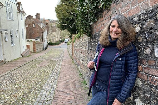 Kate Wood in the left foreground leaning against a flint and brick wall. To her right cobbled Keere Street runs down into the distance.