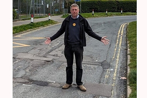 James MacCleary, both hands outstretched, pointing at the many potholes left unfilled in Oakleaf Drive