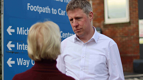 James MacCleary talking to a constituent next to an NHS signboard