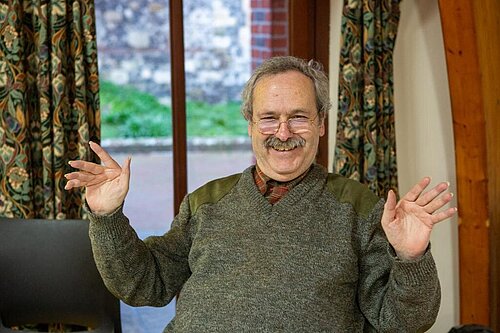 Guy Earl, comfortably dressed, sitting with a big smile and his hands up in an animated gesture .