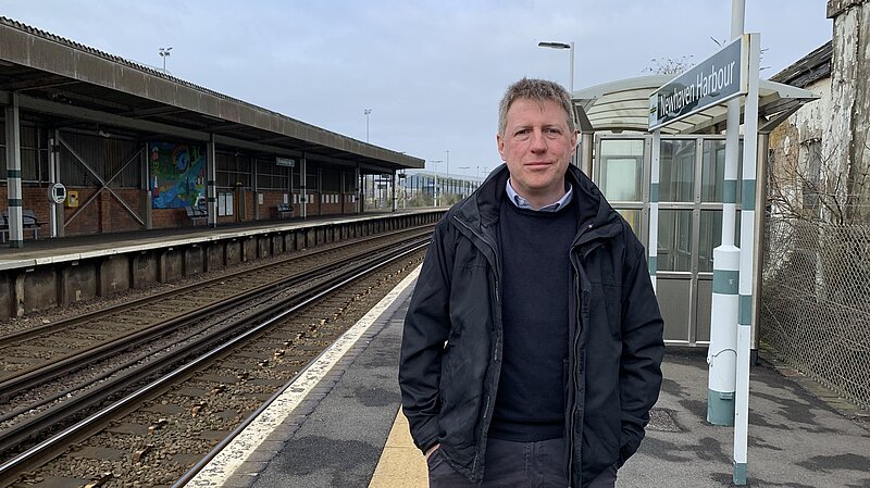 James MacCleary standing on the platform at Newhaven Harbour station. Behind him are empty tracks, station buildings and signalling paraphrenalia