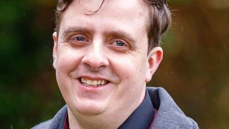 Head and shoulders of Sean Macleod, smiling at the camera, casually dressed with short dark hair.