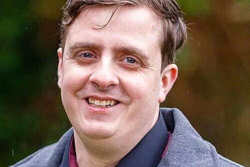 Head and shoulders of Sean Macleod, smiling at the camera, casually dressed with short dark hair.