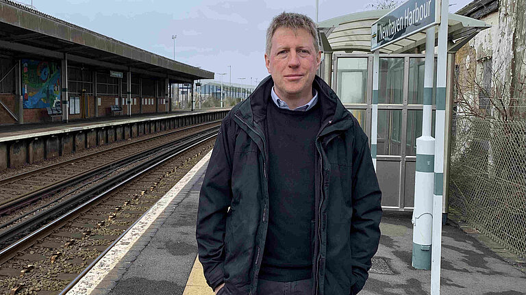 James MacCleary standing on the platform at Newhaven Harbour station. Behind him are empty tracks, station buildings and signalling paraphrenalia
