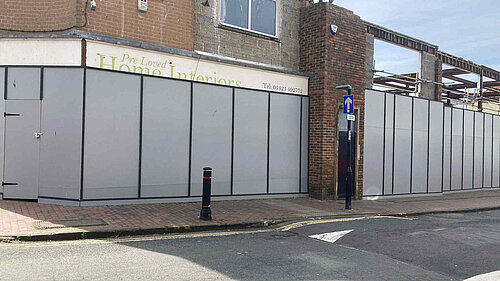 Boarded up facades with one building hollowed out behind, of what used to be a thriving shopping parade