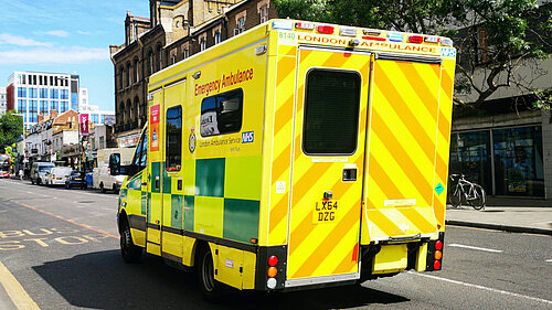 A street scene with a London ambulance in the foreground, taken from the rear.