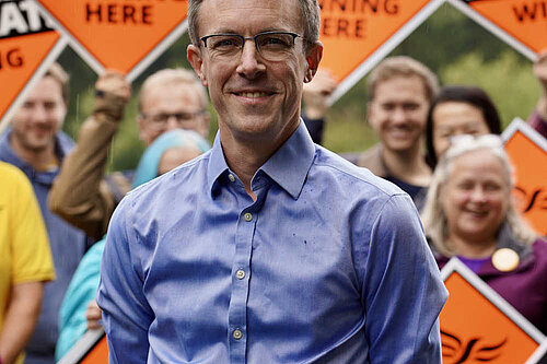 Ben Dempsey in shirtsleeves against a background of posters held by enthusiastic supporters