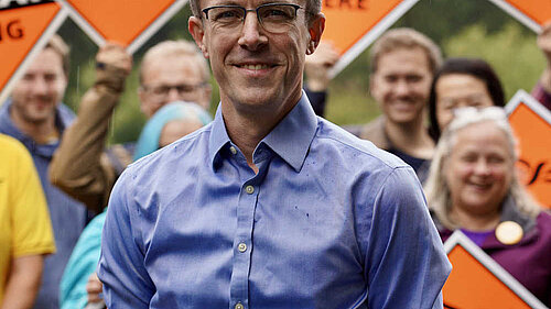 Ben Dempsey in shirtsleeves against a background of posters held by enthusiastic supporters