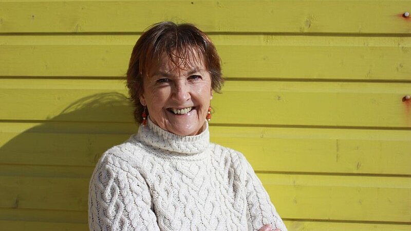 Councillor Carolyn Lambert outside, smiling, against a backdrop of yellow boarding