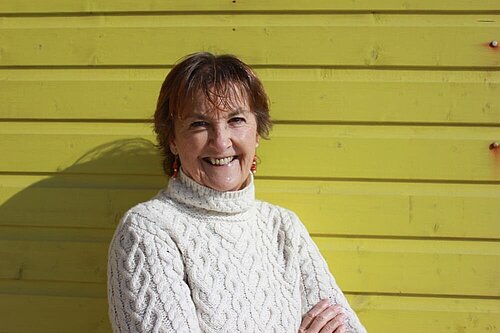 Councillor Carolyn Lambert outside, smiling, against a backdrop of yellow boarding