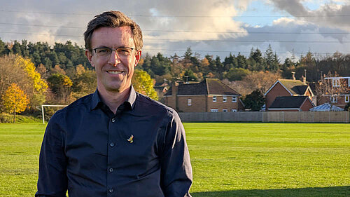 Torso shot of Ben Dempsey in front of a playing field with houses behind it.